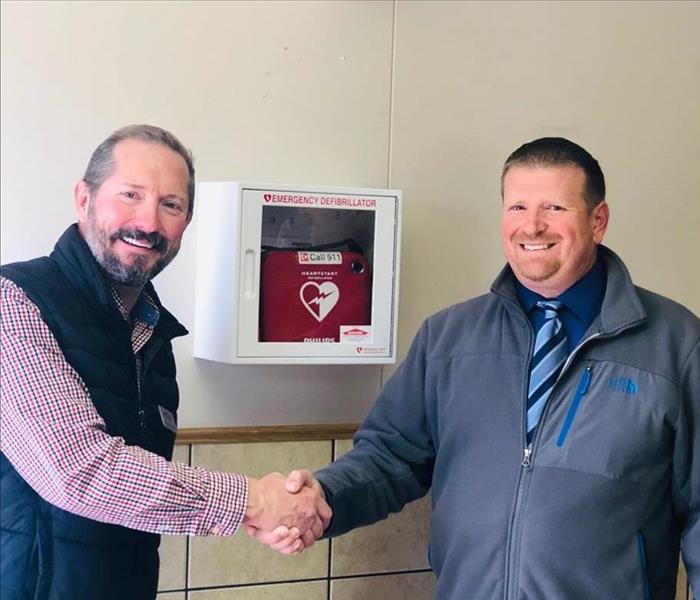 Two men shaking hands infront of a new AED.