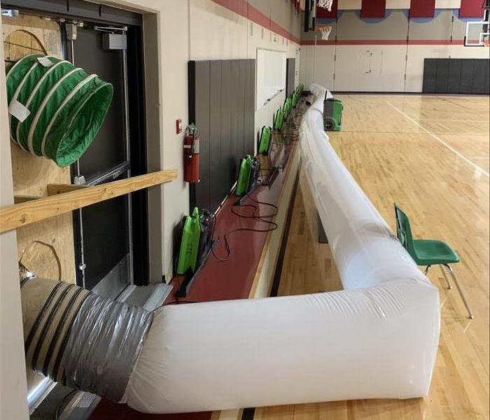 Air movers lined up against a wall in a gym.