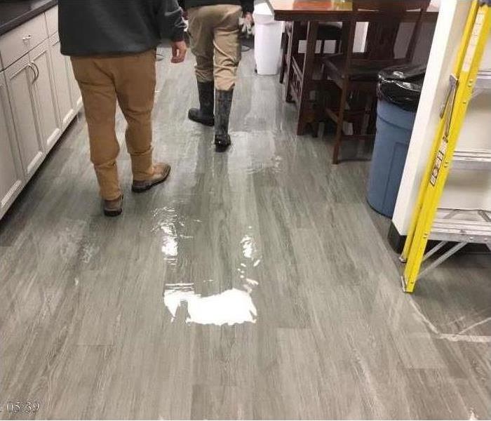 Two people walking by a kitchen floor that has suffered water damage