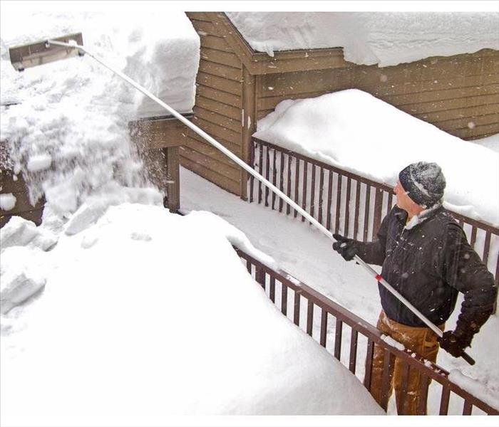 man using a snow rake on garage roof in winter